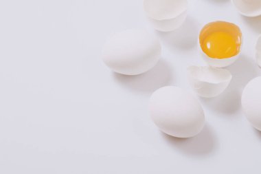 Tam beyaz tavuk yumurtası ve kırık yumurta. Parlak arka planda yumurta sarısı var. Seçici odak.