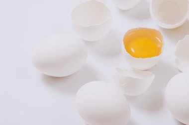 Tam beyaz tavuk yumurtası ve kırık yumurta. Parlak arka planda yumurta sarısı var. Seçici odak.
