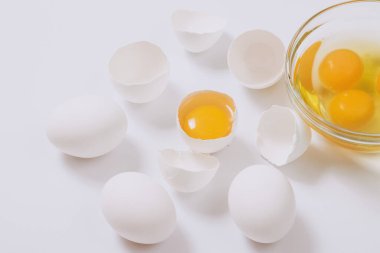 Tam beyaz yumurta ve kırık beyaz yumurta. Yarısı cam kasenin içinde yumurta sarısı ve parlak arkaplanda yumurta akı var. Yaklaş, seçici odaklanma.
