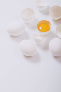 Tam beyaz tavuk yumurtası ve kırık yumurta. Parlak arka planda yumurta sarısı var. Seçici odak.