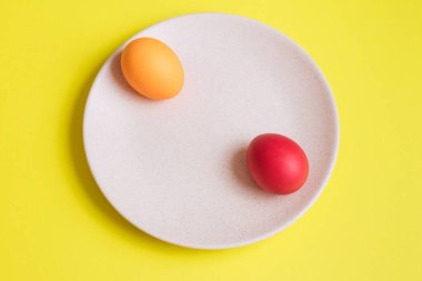 Uzakta seramik tabakta renkli boyanmış yumurtalar. Sarı arka plan. Kavram sahnesi. Paskalya yumurtaları. Seçici odaklanma. Üst görünüm.