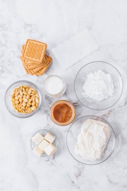 Peynirli kek için malzemeler. Kurabiye, karamel, fıstık, tereyağı, krem peynir, pudra şekeri, cam kaplama krema ve masada jelatin çarşaf. Üst görünüm.