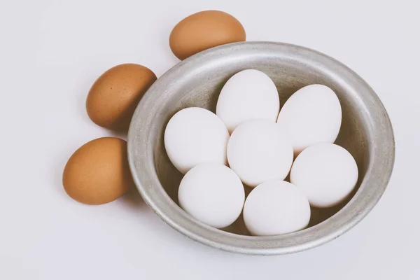 stock image Brown eggs on bright background and white eggs in metal bowl. Close up, selective focus. Concept scene. 