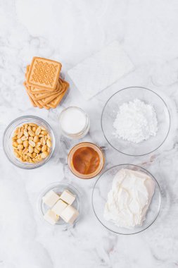 Peynirli kek için malzemeler. Kurabiye, karamel, fıstık, tereyağı, krem peynir, pudra şekeri, cam kaplama krema ve masada jelatin çarşaf. Üst görünüm.