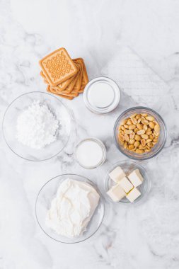 Peynirli kek için malzemeler. Kurabiye, karamel, fıstık, tereyağı, krem peynir, pudra şekeri, cam kaplama krema ve masada jelatin çarşaf. Üst görünüm.