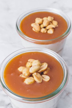 Kavanozda cheesecake. Öğütülmüş kurabiye, karamel, fıstık ve krem peynir katmanları. Karamelaya bulanmış ve fıstıkla süslenmiş. Yakın plan fotoğraf. Seçici odaklanma. Makro çekim.