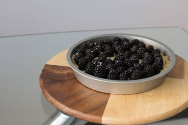 Çilekli cheesecake. Böğürtlenli kek metal formda cam bir masanın üzerinde tahta bir tahta üzerinde.