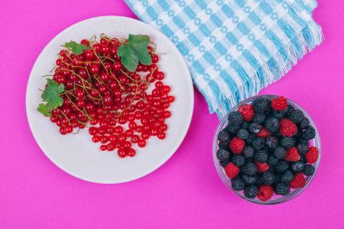 Kırmızı üzümlü seramik tabağın üst görüntüsü ve pembe zemin üzerinde siyah ve kırmızı ahududu olan cam kase..