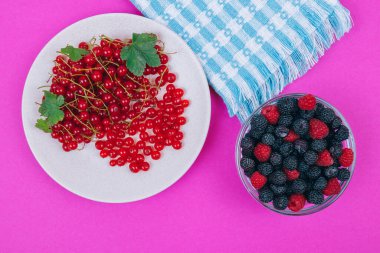 Kırmızı üzümlü seramik tabağın üst görüntüsü ve pembe zemin üzerinde siyah ve kırmızı ahududu olan cam kase..