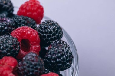 Gri arka planda kırmızı ve siyah ahududu olan cam kaseye yakın plan. Makro çekim.