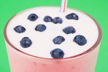 Glass of cold milkshake with fresh blueberries on top. Drink in a glass with a straw on a green background.