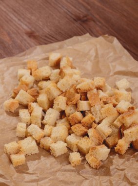 Pieces of roasted white bread at the parchment paper on wooden table. Close-up of delicious croutons.