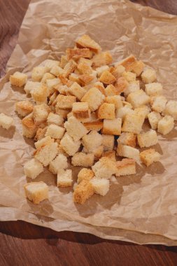 Pieces of roasted white bread at the parchment paper on wooden table. Close-up of delicious croutons.