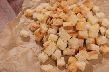 Pieces of roasted white bread at the parchment paper on wooden table. Close-up of delicious croutons.