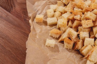 Pieces of roasted white bread at the parchment paper on wooden table. Close-up of delicious croutons.