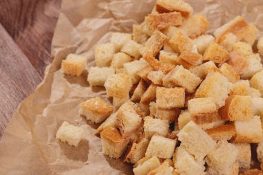 Pieces of roasted white bread at the parchment paper on wooden table. Close-up of delicious croutons.