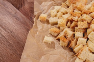 Pieces of roasted white bread at the parchment paper on wooden table. Close-up of delicious croutons.