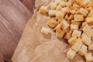 Pieces of roasted white bread at the parchment paper on wooden table. Close-up of delicious croutons.