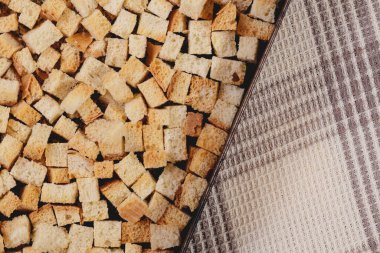 Pieces of roasted white bread in the baking tray on tablecloth. Close-up of delicious croutons.