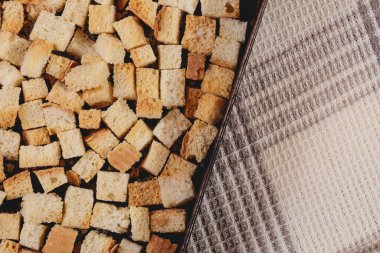 Pieces of roasted white bread in the baking tray on tablecloth. Close-up of delicious croutons.