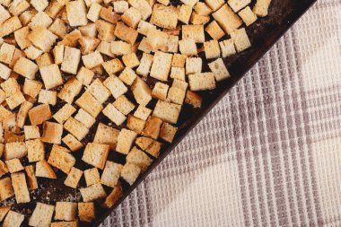Pieces of roasted white bread in the baking tray on tablecloth. Close-up of delicious croutons.