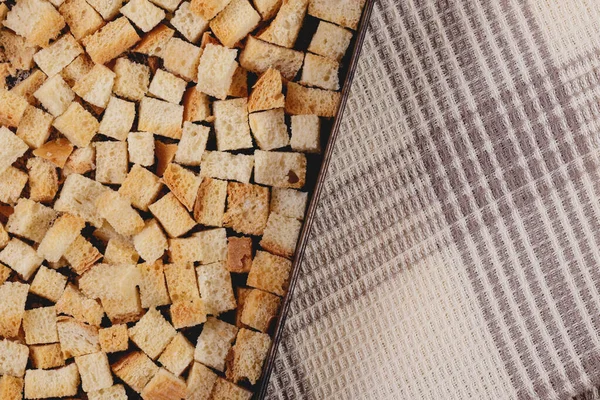 Pieces of roasted white bread in the baking tray on tablecloth. Close-up of delicious croutons.