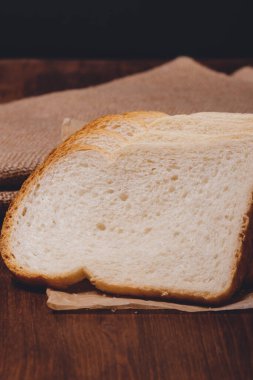 Kahverengi kabuklu dilimlenmiş beyaz ekmek üzerinde çuval bezi olan parşömen kağıdının üzerine yakın plan..