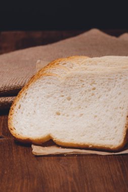 Kahverengi kabuklu dilimlenmiş beyaz ekmek üzerinde çuval bezi olan parşömen kağıdının üzerine yakın plan..