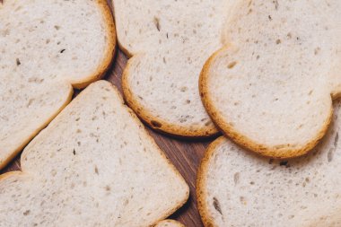 Dilimlenmiş beyaz ekmek. Kahverengi kabuklu. Koyu ahşap masaya yakın. Üst görünüm