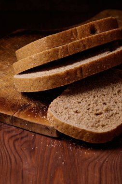 Dilimlenmiş kahverengi ekmek, tahtanın üzerinde, koyu ahşap masada..