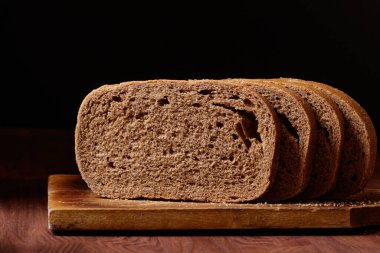 Dilimlenmiş kahverengi ekmek, tahtanın üzerinde, koyu ahşap masada..