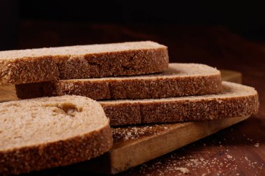 Koyu ahşap masada kepek kaplı dilimlenmiş kahverengi ekmek. Makro çekim.