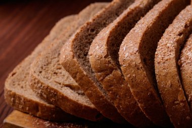 Koyu ahşap masada kepek kaplı dilimlenmiş kahverengi ekmek..