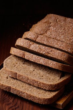 Koyu ahşap masada kepek kaplı dilimlenmiş kahverengi ekmek..