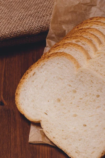 木のテーブルにサッククロスが付いているパッチのペーパーの茶色の粉の閉鎖が付いているスライスされた白いパン — ストック写真