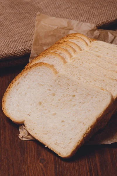 Gesneden Wit Brood Met Bruine Korst Close Perkamentpapier Houten Tafel — Stockfoto