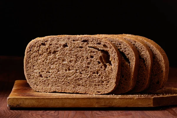 Κομμένο Καφέ Ψωμί Ξύλινη Σανίδα Στο Σκούρο Ξύλινο Τραπέζι — Φωτογραφία Αρχείου