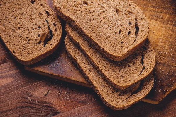 Koyu ahşap masada kepek kaplı dilimlenmiş kahverengi ekmek. Üst görünüm