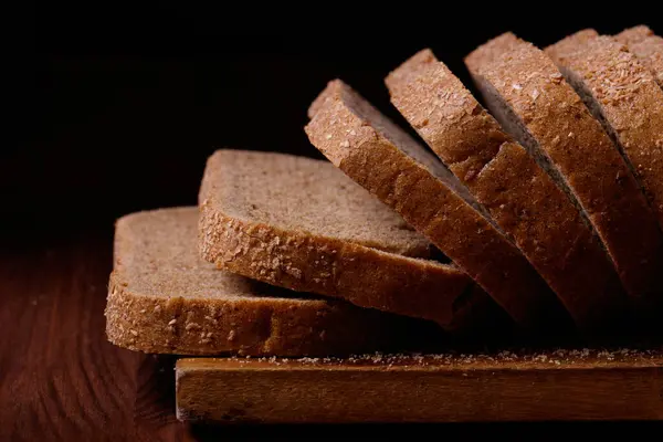 Krájený Hnědý Chléb Pokrytý Otrubami Dřevěné Desce Tmavém Dřevěném Stole — Stock fotografie