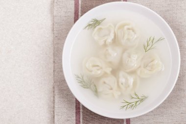 Ev yapımı pelmeni ve taze dereotlu Bouillon. Hamur köfteli çorba ve masa örtüsü üzerine otlar. Üst görünüm