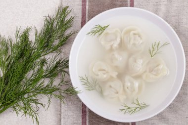 Ev yapımı pelmeni ve taze dereotlu Bouillon. Hamur köfteli çorba ve masa örtüsü üzerine otlar. Üst görünüm