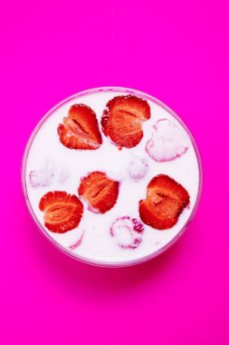 Pembe arka planda çilekli yoğurtlu cam kâse manzarası. Taze çilek dilimleriyle kaplı çilekli yoğurt.. 