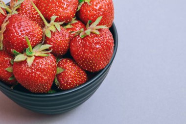 Olgun çilek. Gri arka planda çilekli siyah kase. Çilek kapağı..