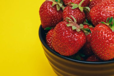 Olgun çilek. Sarı arka planda çilekli siyah kase. Çilek kapağı..