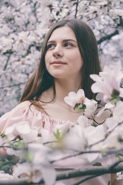 Manolya çiçekleri içinde güzel bir genç kadının yakın plan portresi. Manolya çiçekli bahar kızı. Pembe elbiseli esmer kızın portresi..