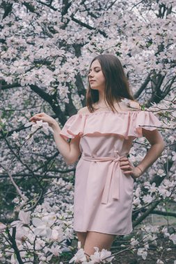 Manolyalı beyaz çiçekli bahar kızı. Manolya çiçekleriyle çevrili pembe elbiseli esmer kız..