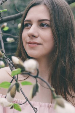 Manolya çiçekleri içinde güzel bir genç kadının yakın plan portresi. Manolya çiçekli bahar kızı. Pembe elbiseli esmer kızın portresi..
