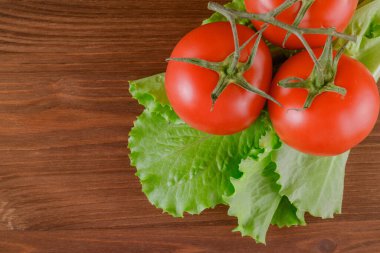Taze, olgun kırmızı domates ve marul. Ahşap masada bir set marul ve domates dalı uzanıyor. - Yakın çekim. Üst görünüm.