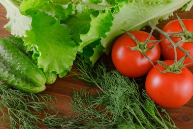 Birkaç salatalık, dereotu, marul, domates dalı ahşap masada yatıyor. Taze çiğ organik sebzeler..