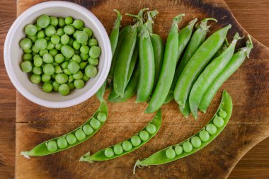 Taze bezelye ve bezelye kabukları. Kavanozda bezelye ve tahta tahtada bezelye kabukları. Üst görünüm.